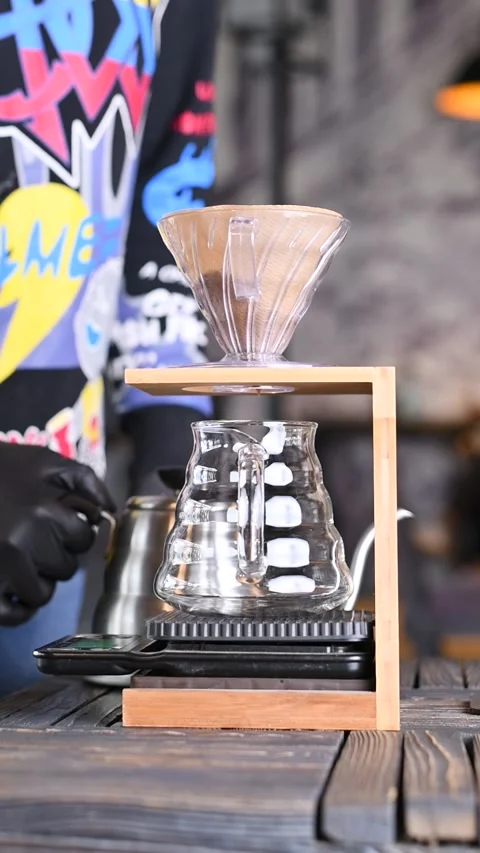 Clear glass server sitting under a transparent V60 dripper in a minimalist woode Video stock 309656264