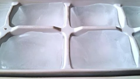 Clear ice cubes resting inside a white plastic tray container Stock Photos