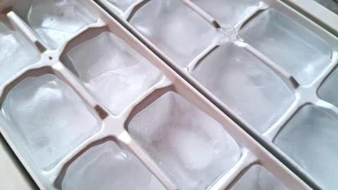 Clear ice cubes sitting inside a white plastic tray container Stock Photos