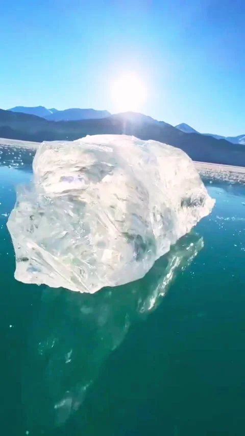 Clear iceberg floating on turquoise glacial water with mountain scenery in .. 库存影片 333607068