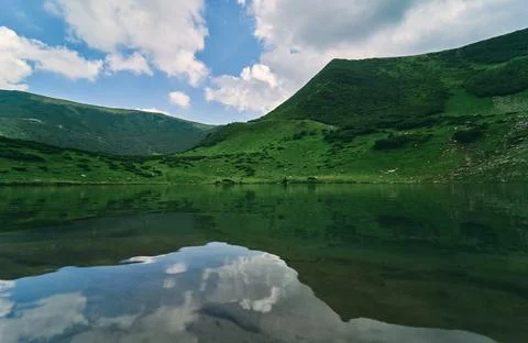 Clear lake against the backdrop of green mountains and blue sky in sunny summ Stock-Fotos