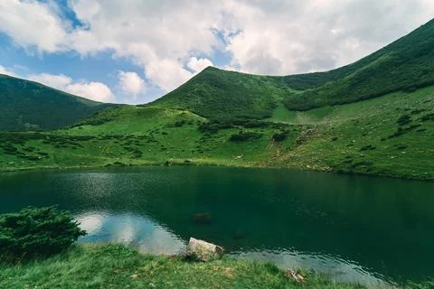 Clear lake against the backdrop of green mountains and blue sky in sunny summ Stock Photos