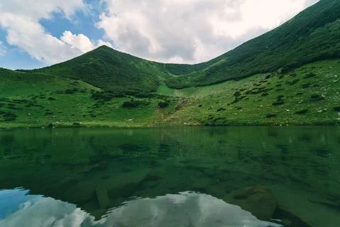 Clear lake against the backdrop of green mountains and blue sky in sunny summ Stock Photos