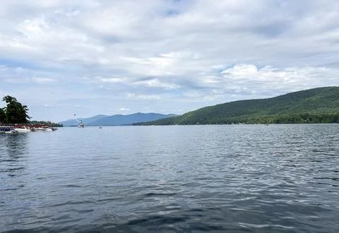 Clear Lake Under a Cloudy Sky Near Green Mountains Stock Photos