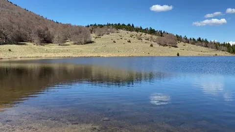 Clear lake water reflecting mountain trees under blue sky in les Cévennes Stock Footage 340640045