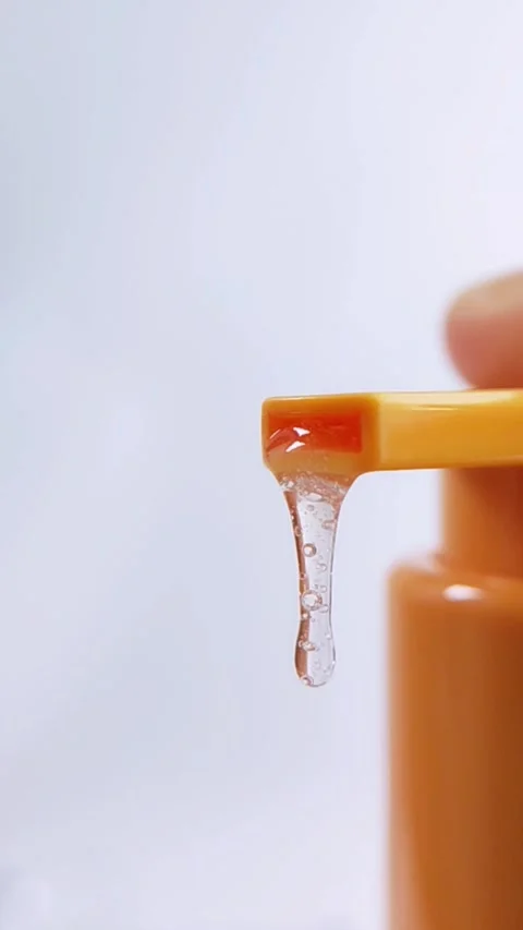 Clear liquid dripping slowly from orange product packaging. Vertical close .. Stock Footage 336238756