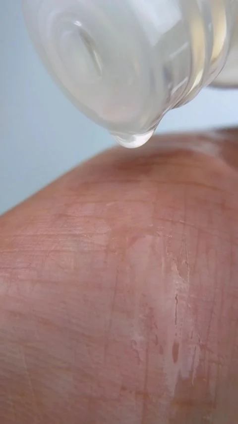 Clear liquid droplets dripping onto hand skin, looking shiny and glossy Vídeo Stock 334874609