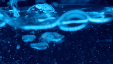 Clear liquid pouring under blue light with swirling particles Stock Footage 114085707