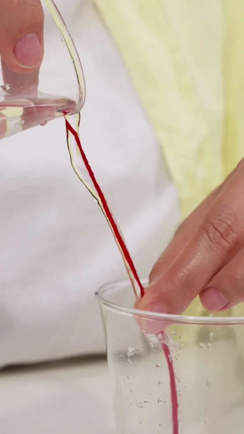 Clear liquid pours down red string into glass jar Stock Footage 331769953