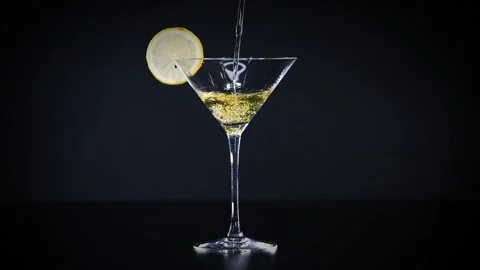 Clear martini glass with lemon slice receiving a steady stream of golden li.. Stock Footage 334102752