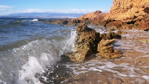 Clear ocean waves crashing against a rugged rocky coastal shoreline Stock Footage 337410261
