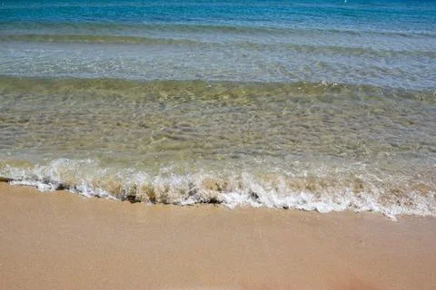 Clear ocean waves gently lap against sandy beach shoreline Stock Photos