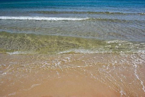 Clear ocean waves gently lapping on sandy beach under bright sunlight Фото