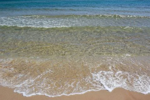 Clear ocean waves gently lapping on sandy beach under bright sunlight Stock Photos
