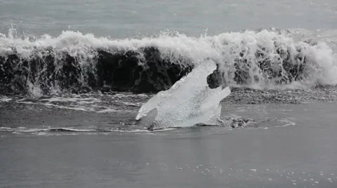 Clear peace of ice hit by the waves on the black sand beach in Iceland Stock Footage 33778558