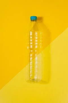 Clear plastic bottle with blue cap on a yellow background. Recycling and envi Stock Photos