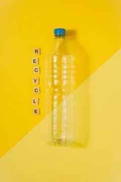 Clear plastic bottle with blue cap on a yellow background and the word recycle Stock Photos