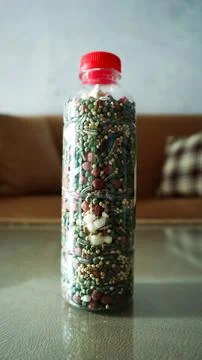 A clear plastic bottle with a red cap filled with colorful hamster food,  s.. Stock Photos