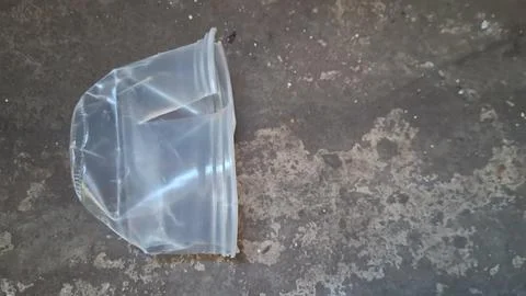 Clear plastic container discarded on a rough dark concrete floor surface Stock Photos