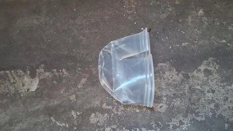 Clear plastic container discarded on a rough dark concrete floor Stock Photos