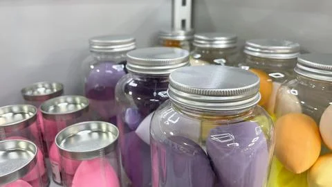 Clear plastic jars with silver lids filled with colorful makeup sponges on .. 스톡 사진