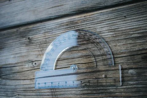 Clear plastic protractor with integrated ruler rests on weathered. Stock Photos