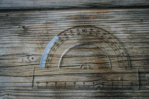 Clear plastic protractor with integrated ruler rests on weathered. Stock Photos