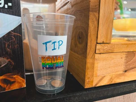 Clear plastic tip jar with "TIP" written in blue and "EQUAL FOR ALL" in rai.. Stock Photos