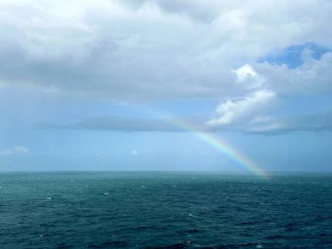 A clear rainbow in the middle of the ocean breaking through the clouds into the  Stock Photos