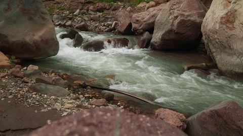 Clear river flows between large rocks in serene natural setting with surrounding 動画素材 313107717