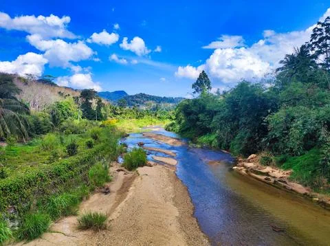 Clear river flows through green landscape under blue sky with clouds. Namto.. Stock Photos