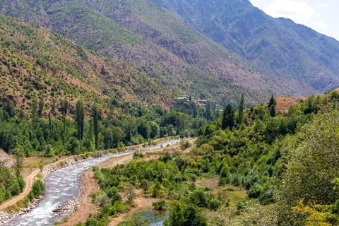A clear river flows through a lush green valley surrounded by rugged, tree-.. 스톡 사진