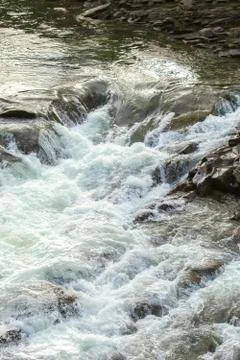 Clear river with rocks leads towards mountains, small waterfall. Stock Photos