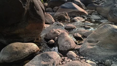 Clear river stream flowing around large boulders in natural sunlight Stock Footage 344087953