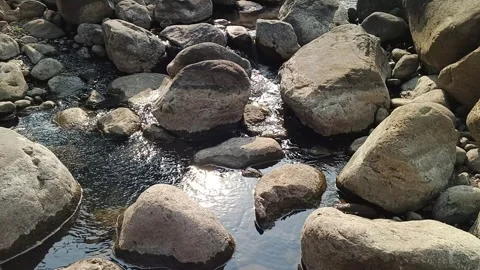 Clear river stream flowing gently between large natural boulders under brigh Stock Footage 344087440