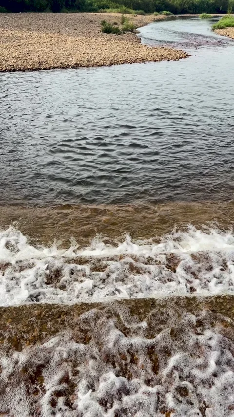 Clear river water cascading over steps with a rocky riverbank in background. Stock Footage 346013096