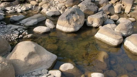 Clear river water flowing around large sunlit boulders in a rocky stream bed Stock Footage 342957738