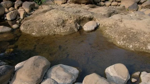 Clear river water gently flowing through a pool of smooth, weathered boulder Stock Footage 342957752