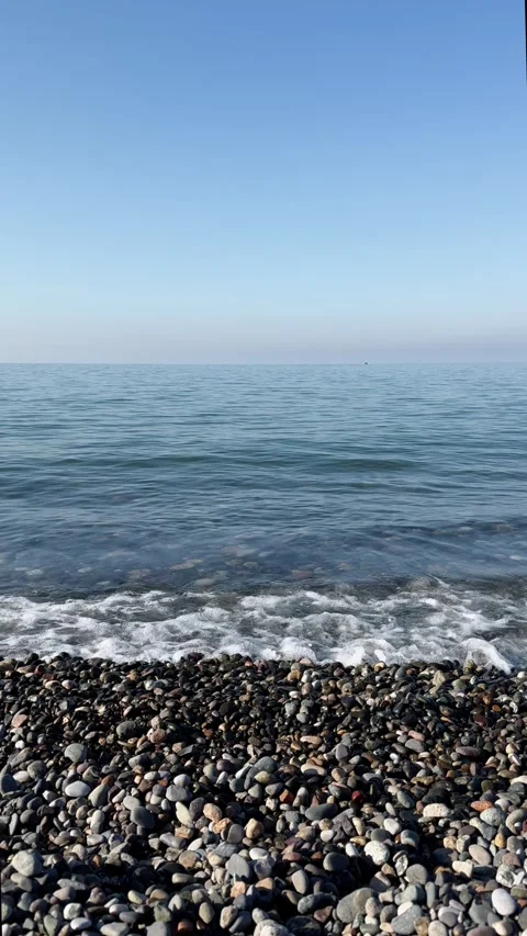 Clear sea with small ripples lapping colorful pebble beach under blue sky Stock Footage 305669755