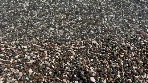 Clear shallow seawater gradually washes over smooth multicolored pebbles along 動画素材 346757269