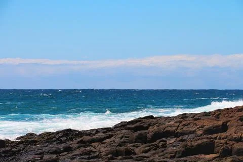 Clear sky and rolling waves create a tranquil coastal view with rocky shore.. Stock Photos