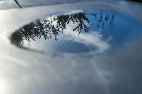 Clear sky reflection in a small water puddle on a glossy dark surface 库存照片