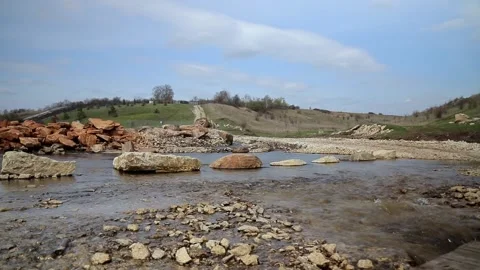 Clear spring water flows over rocks and fall into the river with hills back 動画素材 169719981