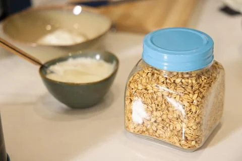 Clear square plastic jar filled with rolled oats sitting on white countertop Stock Photos