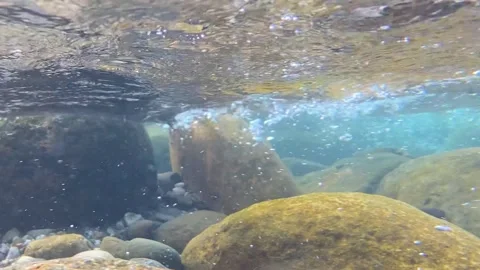 Clear stream flowing through submerged rocks with bubbles underwater at Stock Footage 333822859