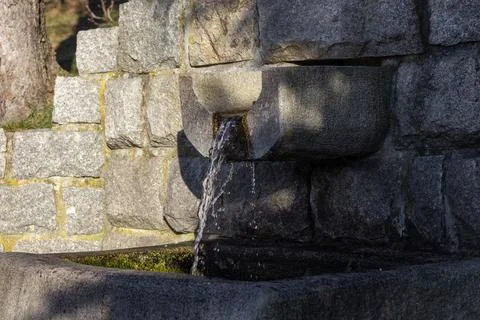 A clear stream of fresh water flows from a rustic granite stone fountain basin, Фото