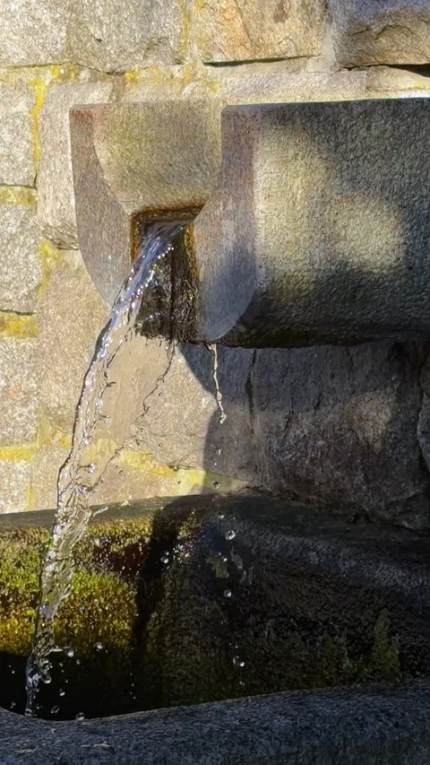 Clear stream of water flowing from a rustic stone fountain in a sunny park Stock Footage 345746240