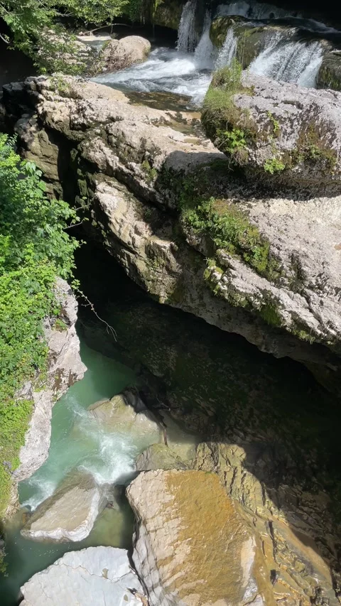 Clear turquoise river rushes beneath layered limestone shelves in a shaded .. Stock Footage 340559233