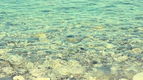 Clear turquoise water gently laps against a smooth stone in a  coastal setting Stock Footage 344810697