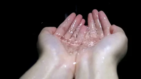 Clear water falls into cupped hands against black background Video stock 332284307